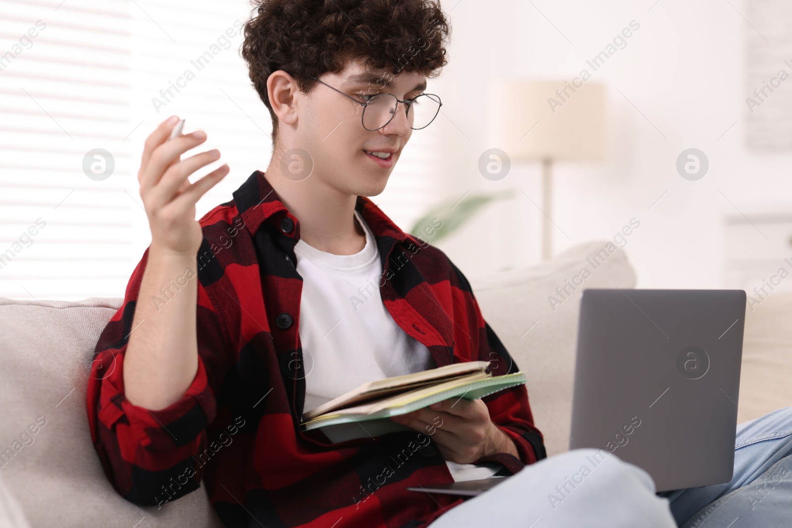 Photo of Teenager with notebooks and pen working on laptop at home. Remote job