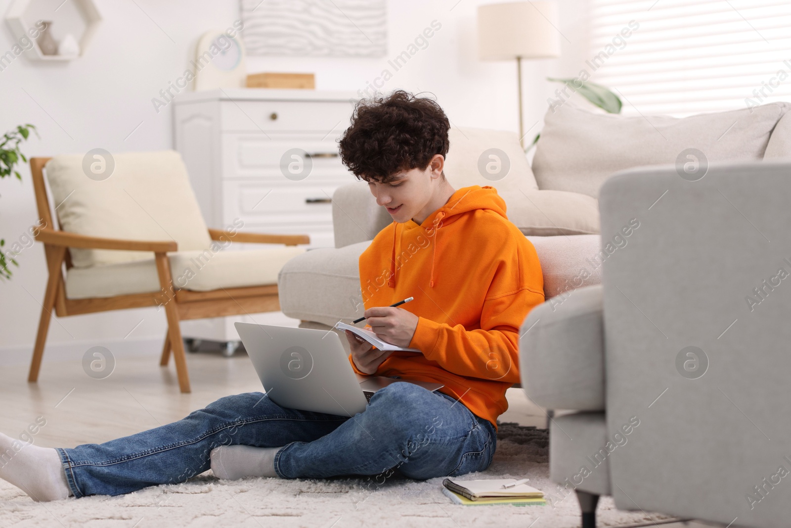 Photo of Teenager taking notes while working with laptop at home. Remote job