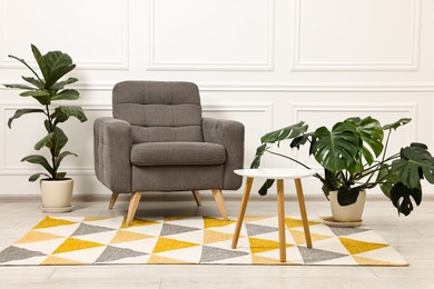 Soft armchair, coffee table and houseplants in stylish room