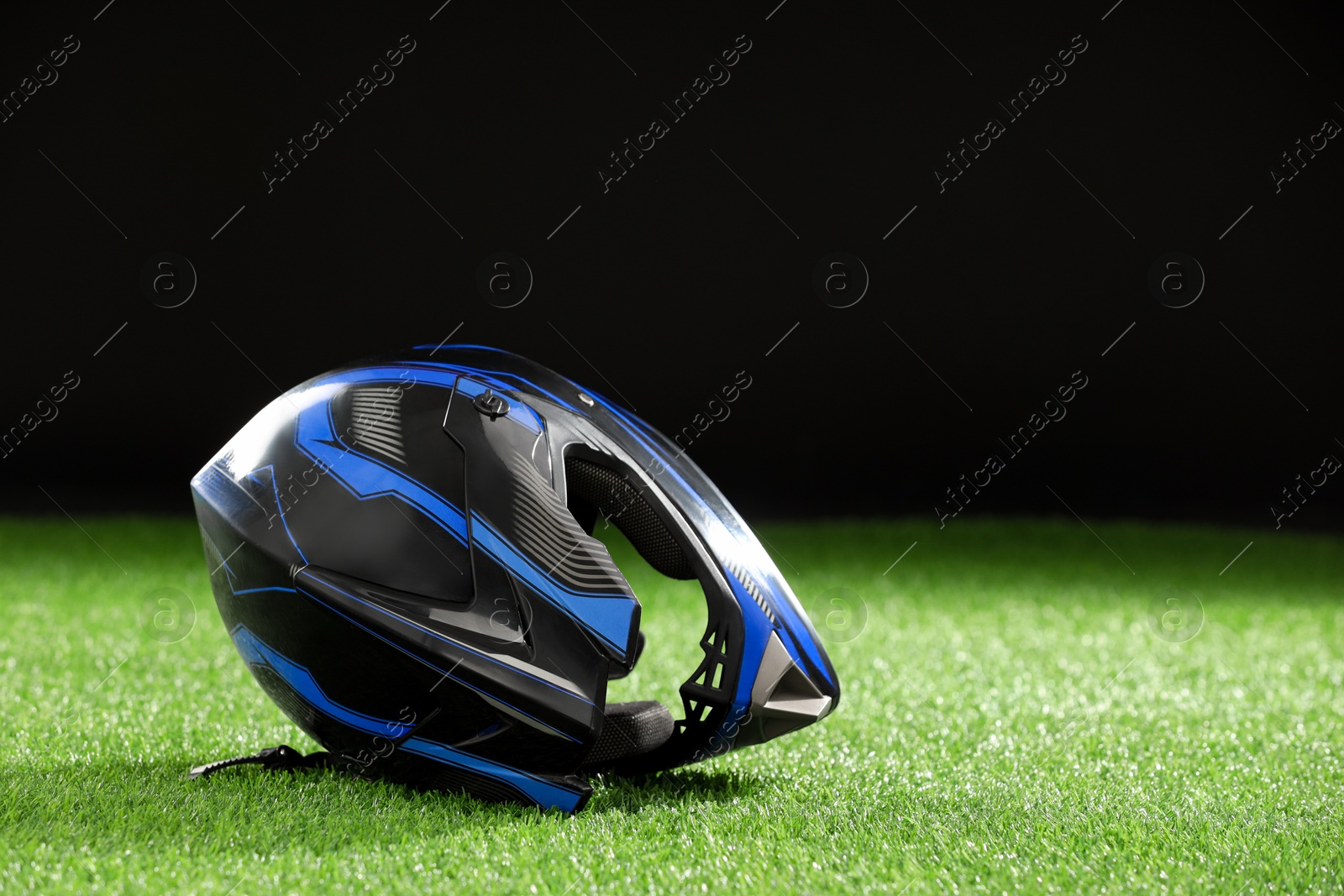 Photo of Modern motorcycle helmet with visor on green grass against black background, space for text