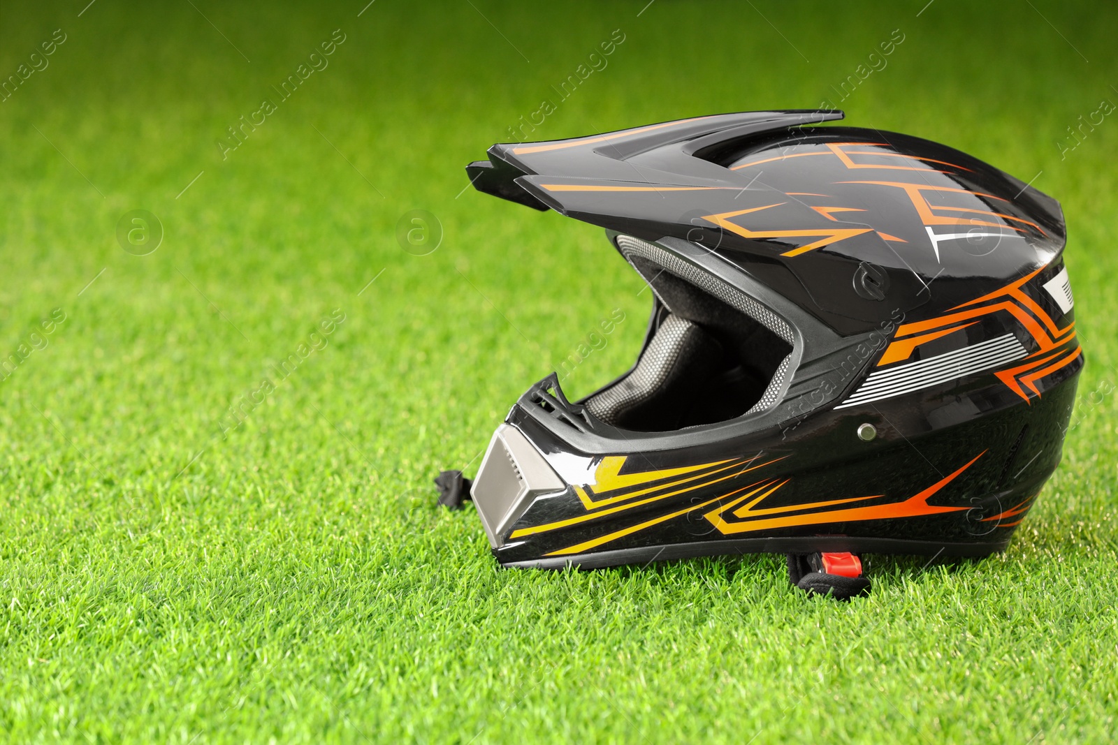 Photo of Modern motorcycle helmet with visor on green grass, space for text