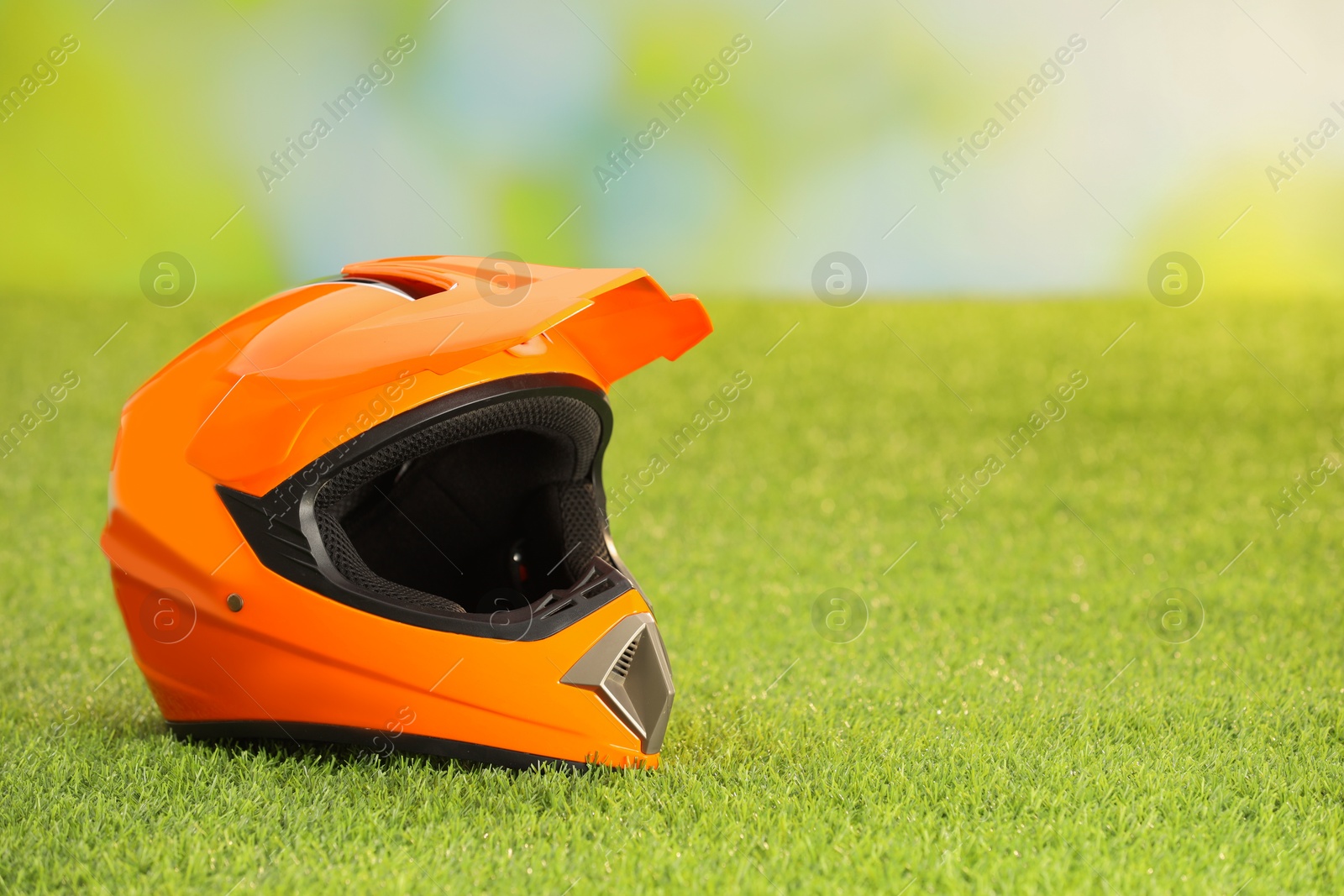 Photo of Orange motorcycle helmet with visor on green grass, space for text