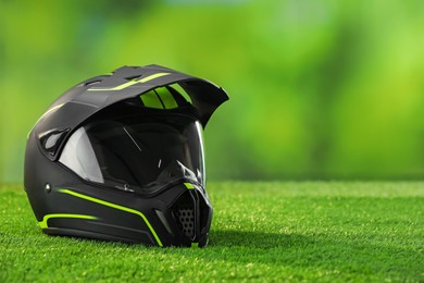 Photo of Modern motorcycle helmet with visor on green grass, space for text