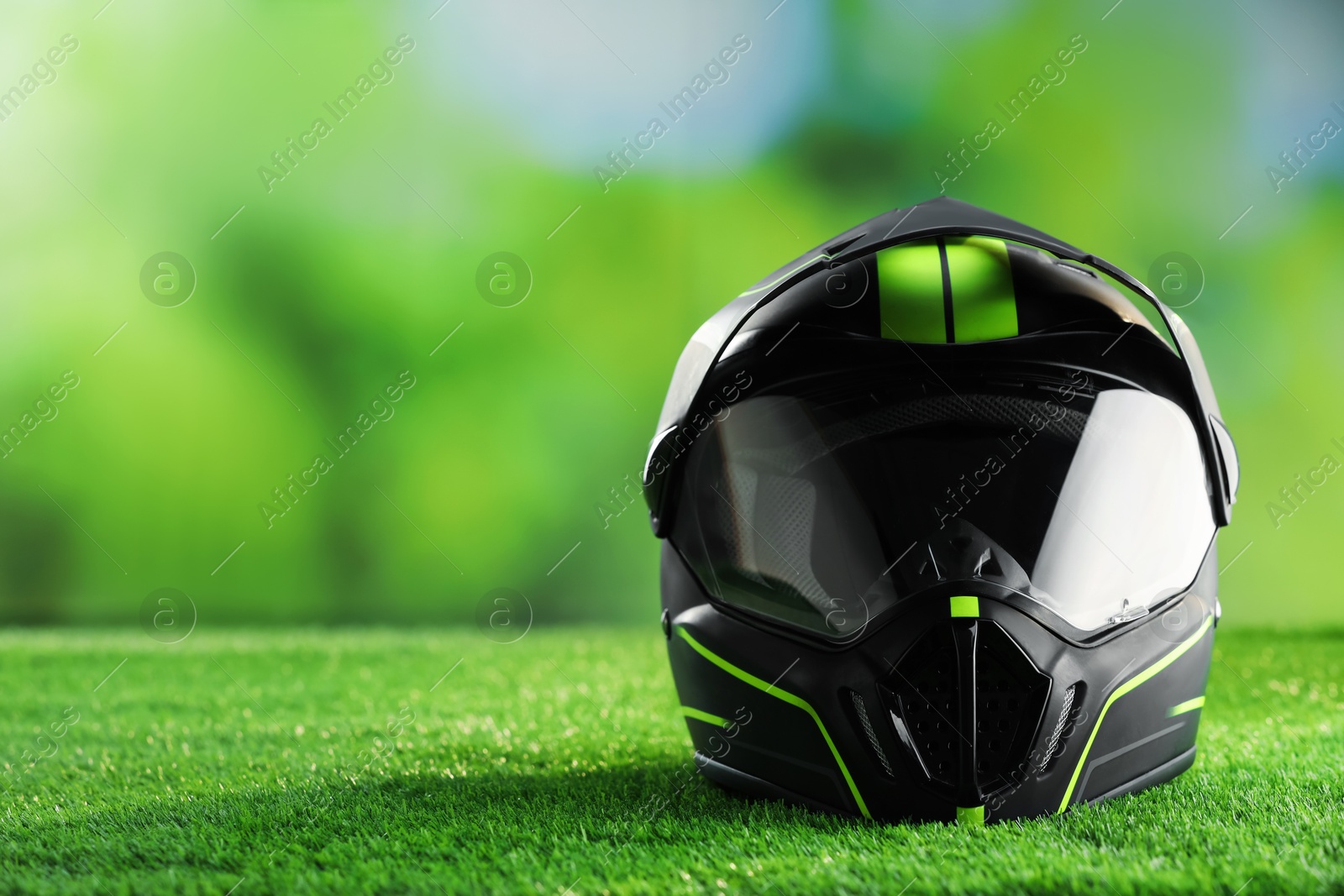 Photo of Modern motorcycle helmet with visor on green grass, space for text