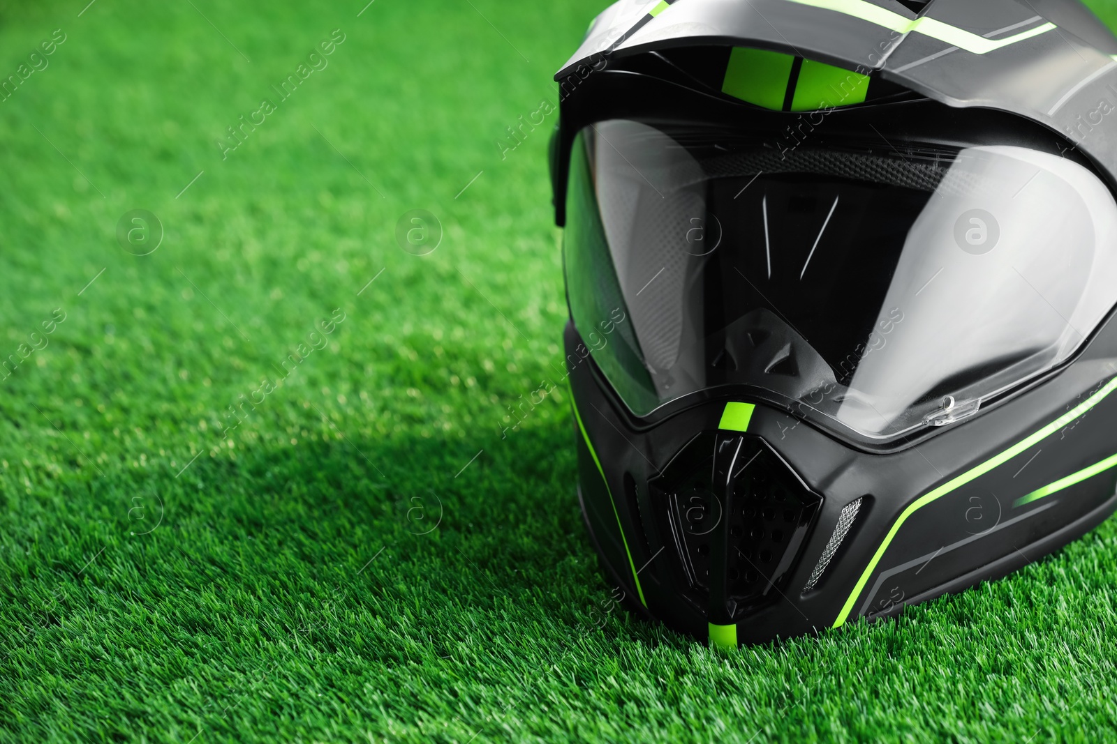 Photo of Modern motorcycle helmet with visor on green grass, closeup. Space for text