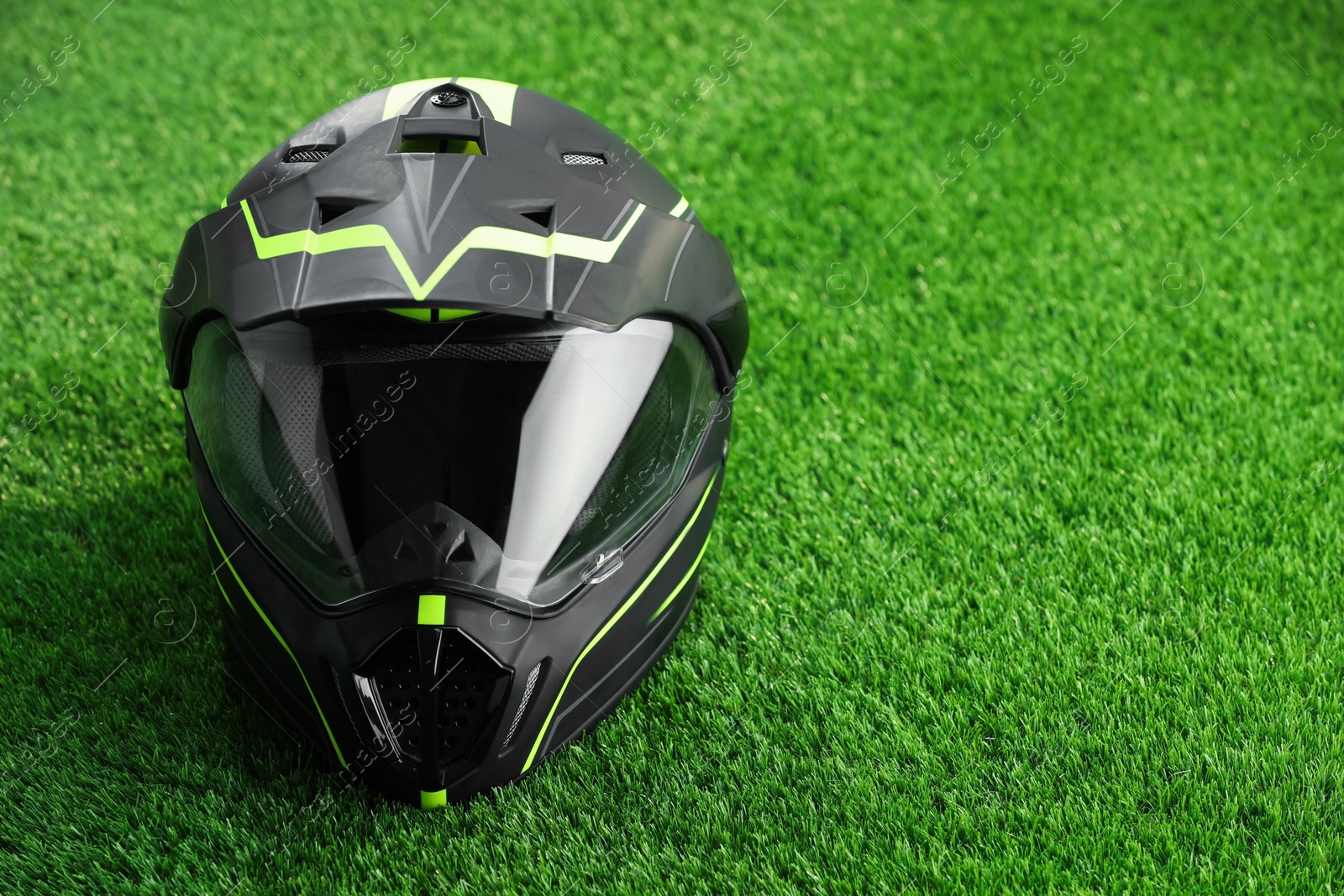 Photo of Modern motorcycle helmet with visor on green grass, space for text