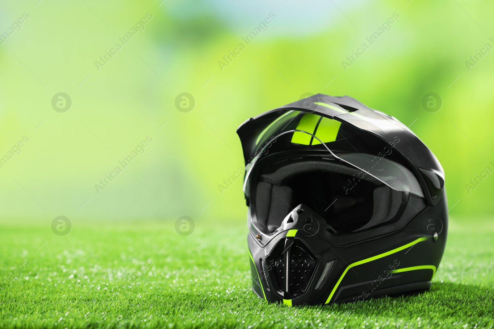 Photo of Modern motorcycle helmet with visor on green grass, space for text