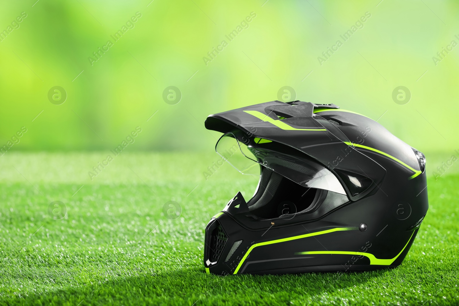 Photo of Modern motorcycle helmet with visor on green grass, space for text