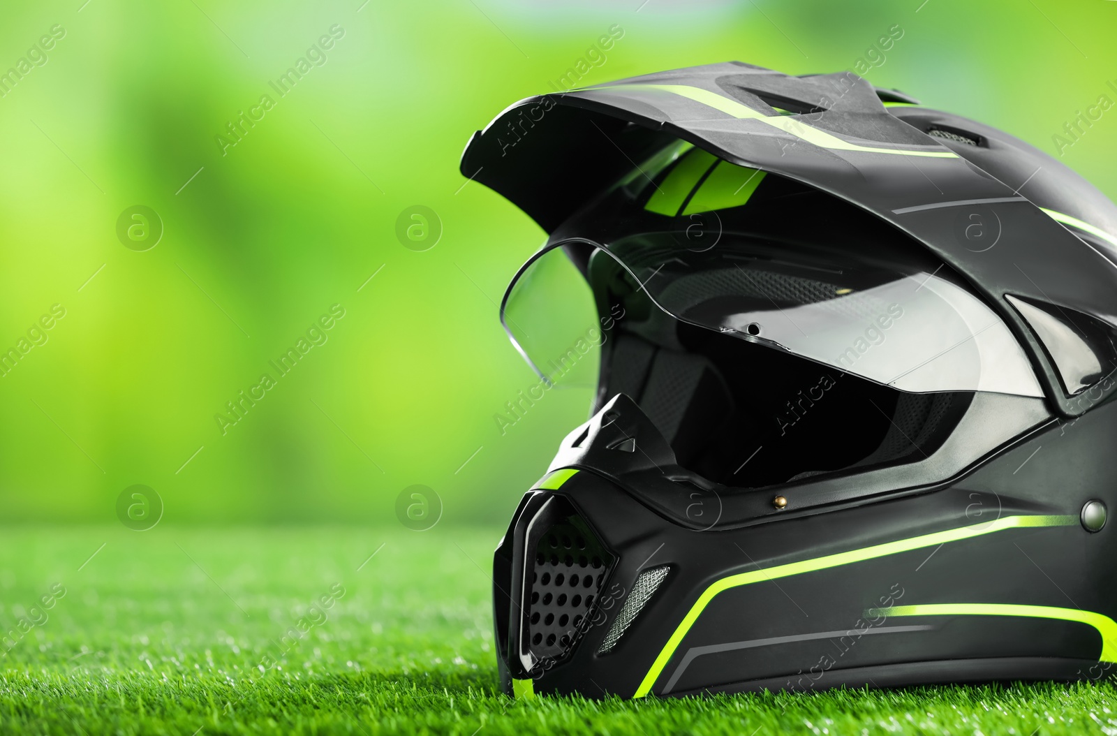 Photo of Modern motorcycle helmet with visor on green grass, closeup. Space for text