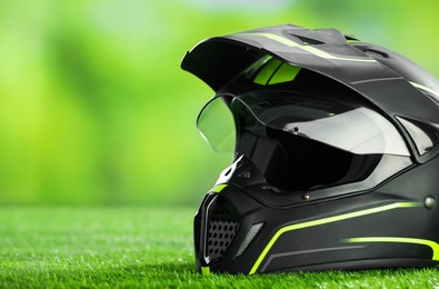 Photo of Modern motorcycle helmet with visor on green grass, closeup. Space for text