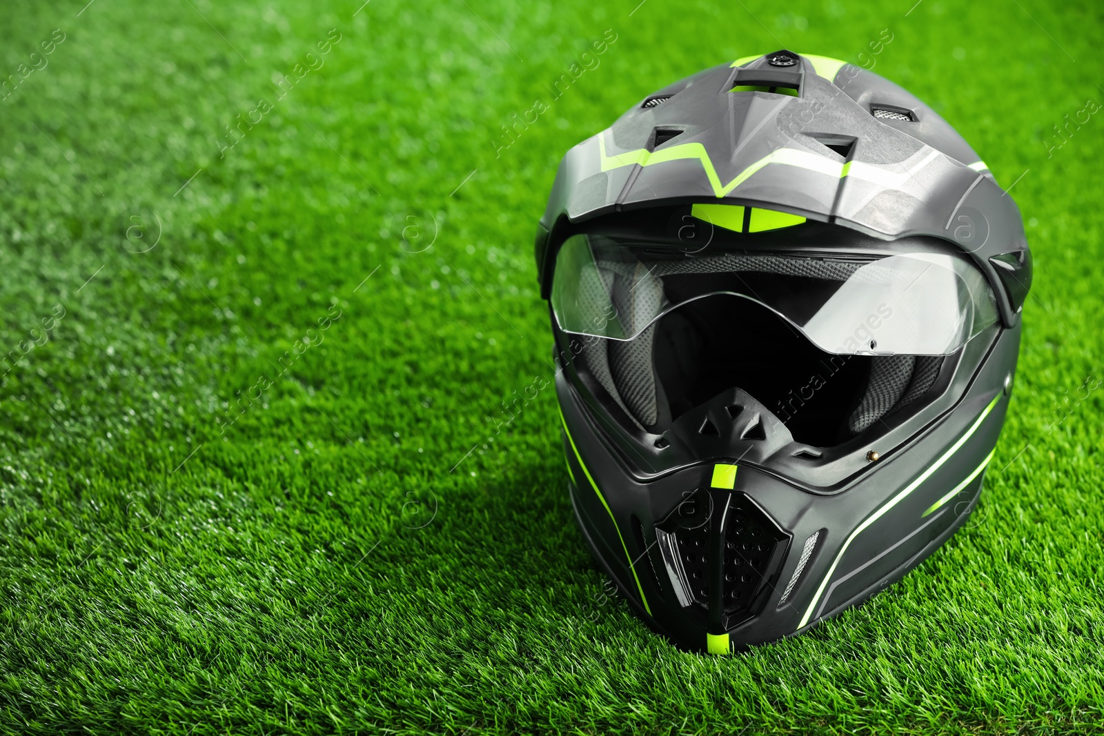 Photo of Modern motorcycle helmet with visor on green grass, space for text