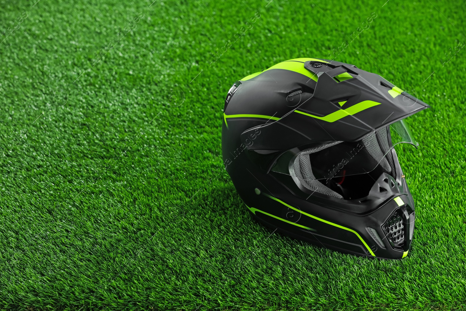 Photo of Modern motorcycle helmet with visor on green grass, space for text