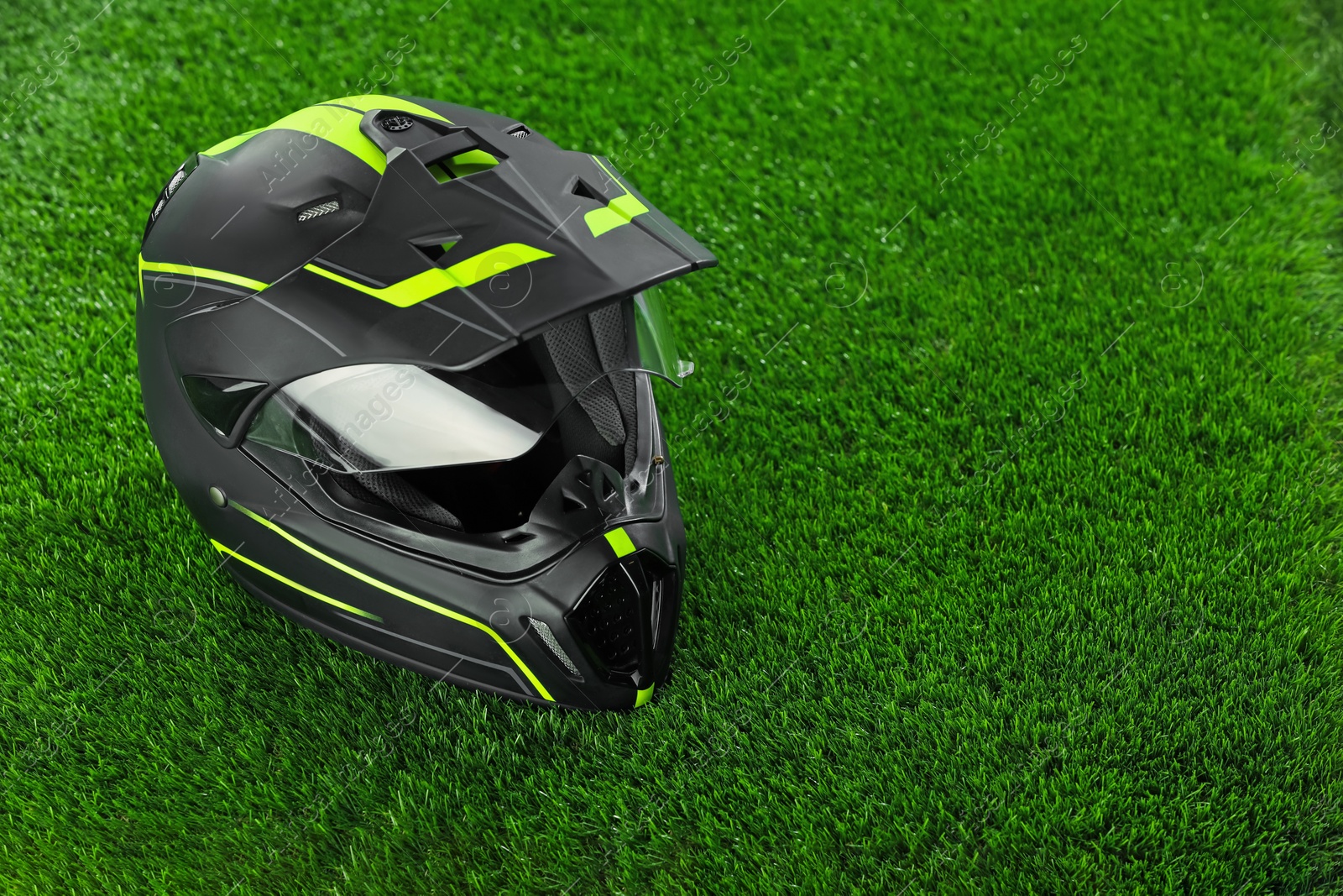 Photo of Modern motorcycle helmet with visor on green grass, space for text