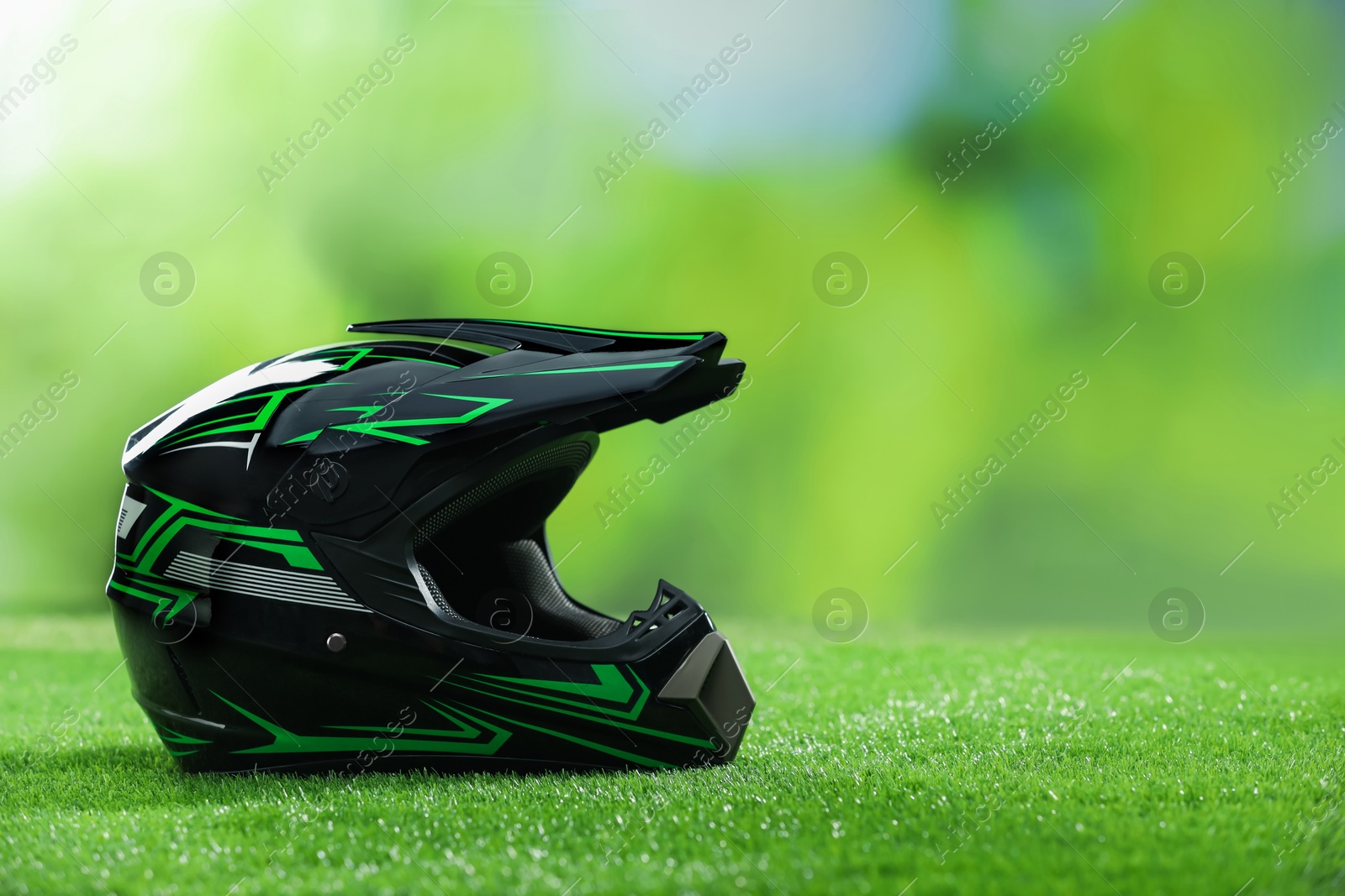 Photo of Modern motorcycle helmet with visor on green grass, space for text