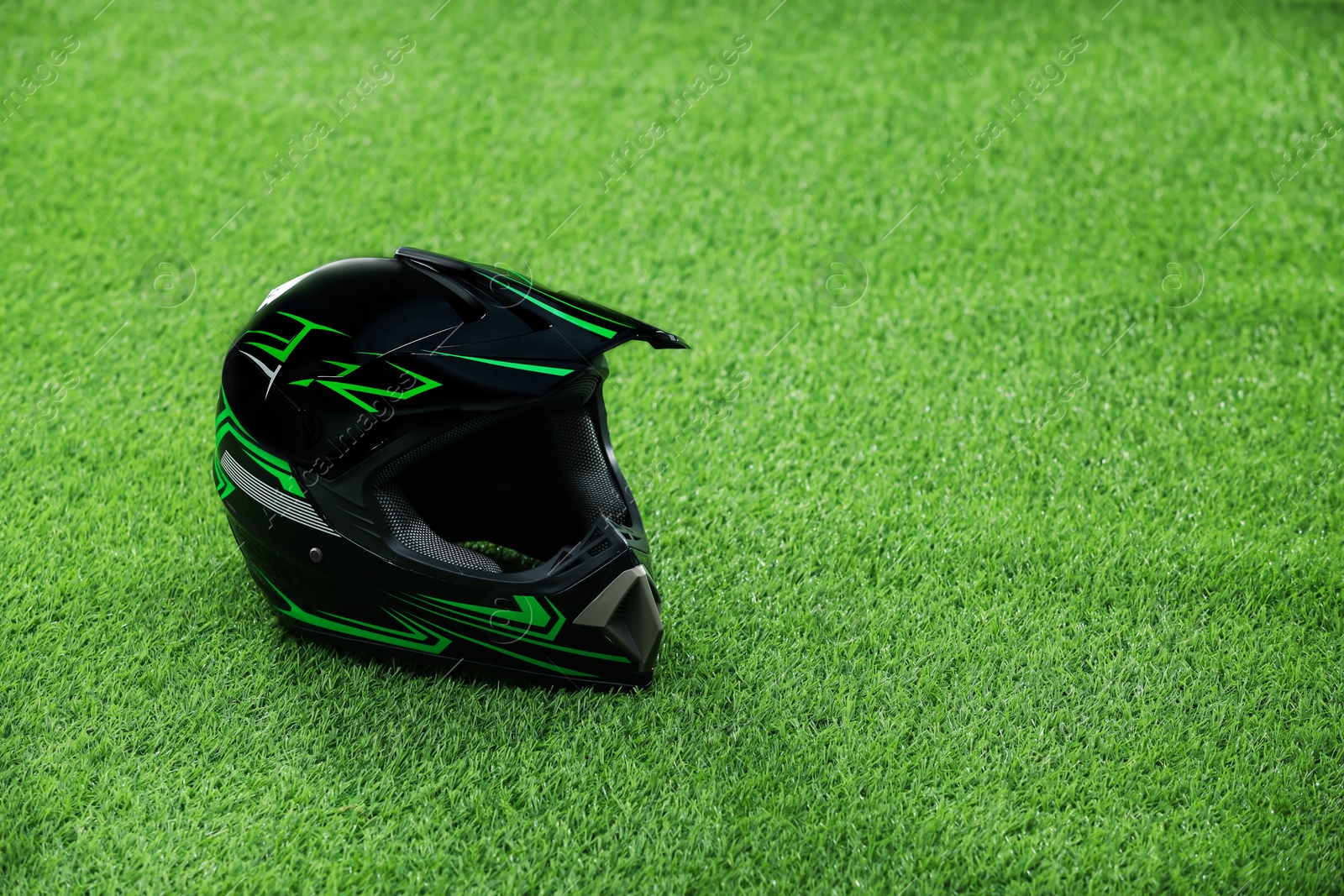 Photo of Modern motorcycle helmet with visor on green grass, space for text