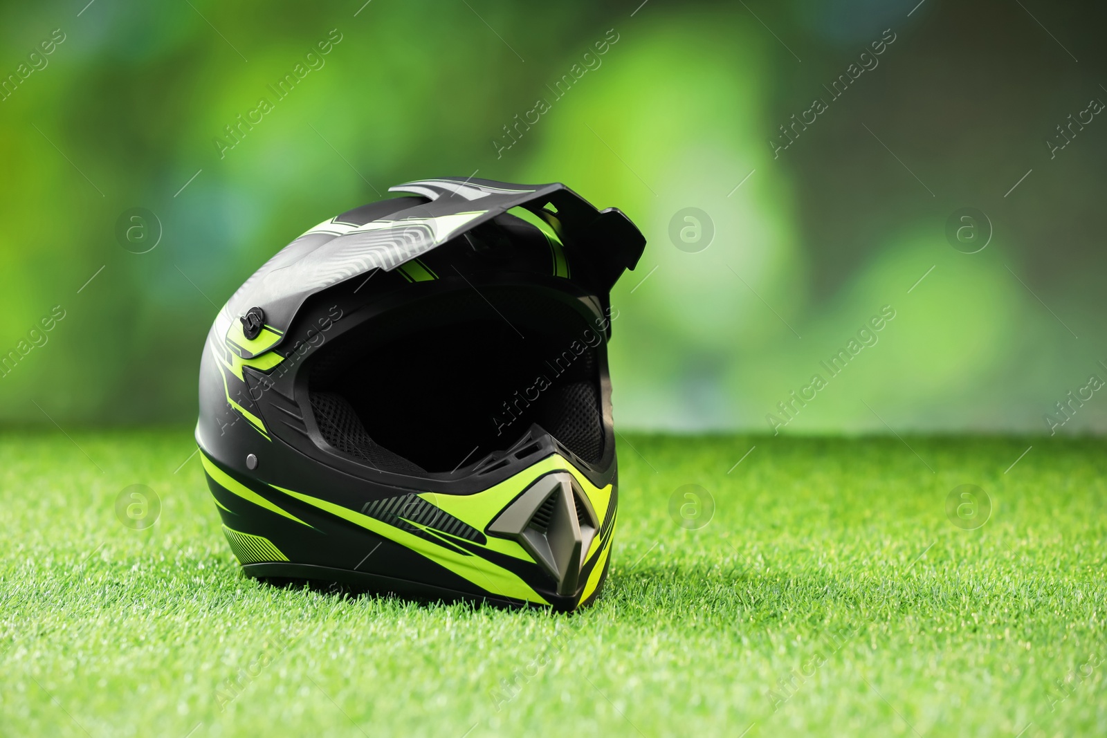 Photo of Modern motorcycle helmet with visor on green grass, space for text