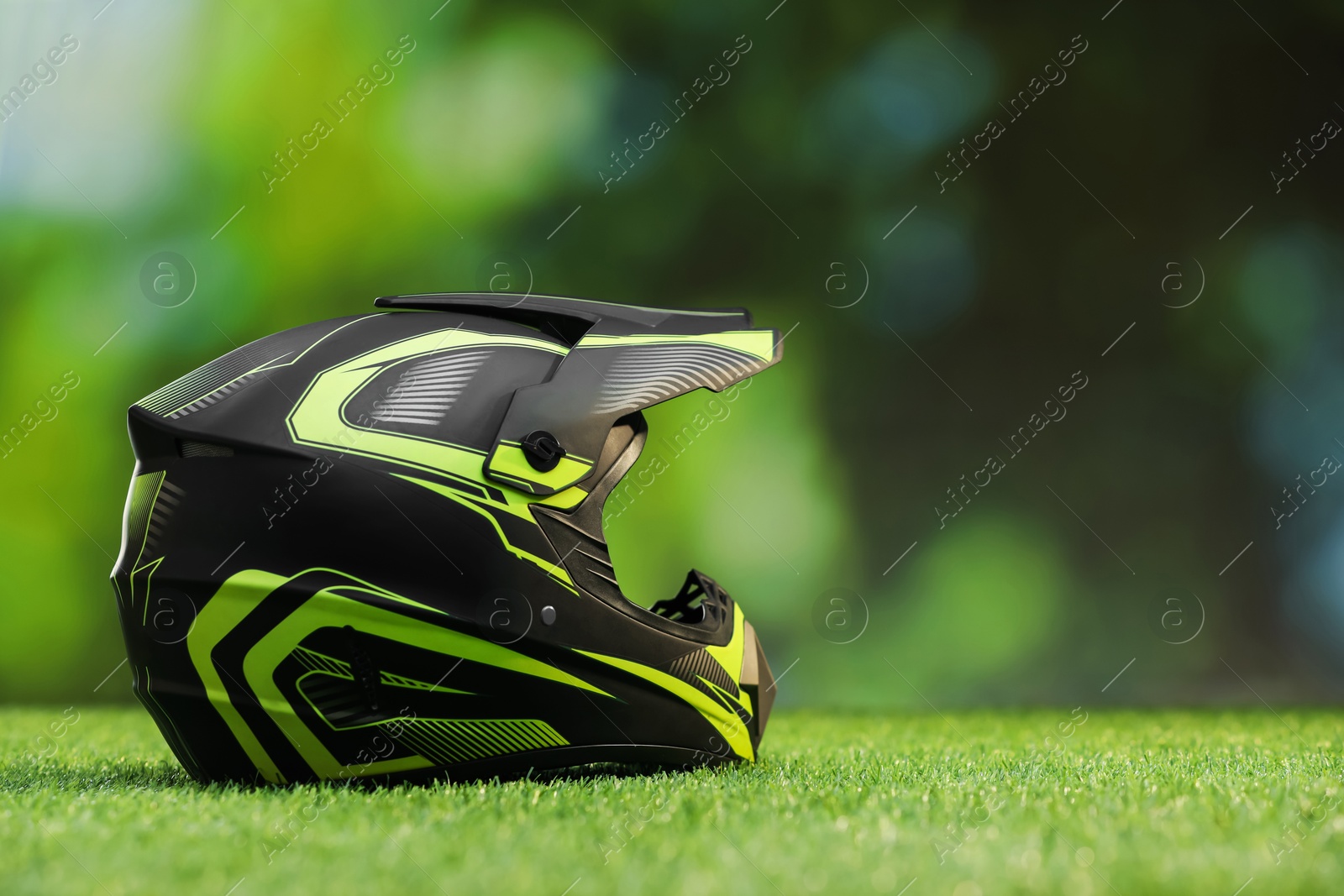 Photo of Modern motorcycle helmet with visor on green grass, space for text