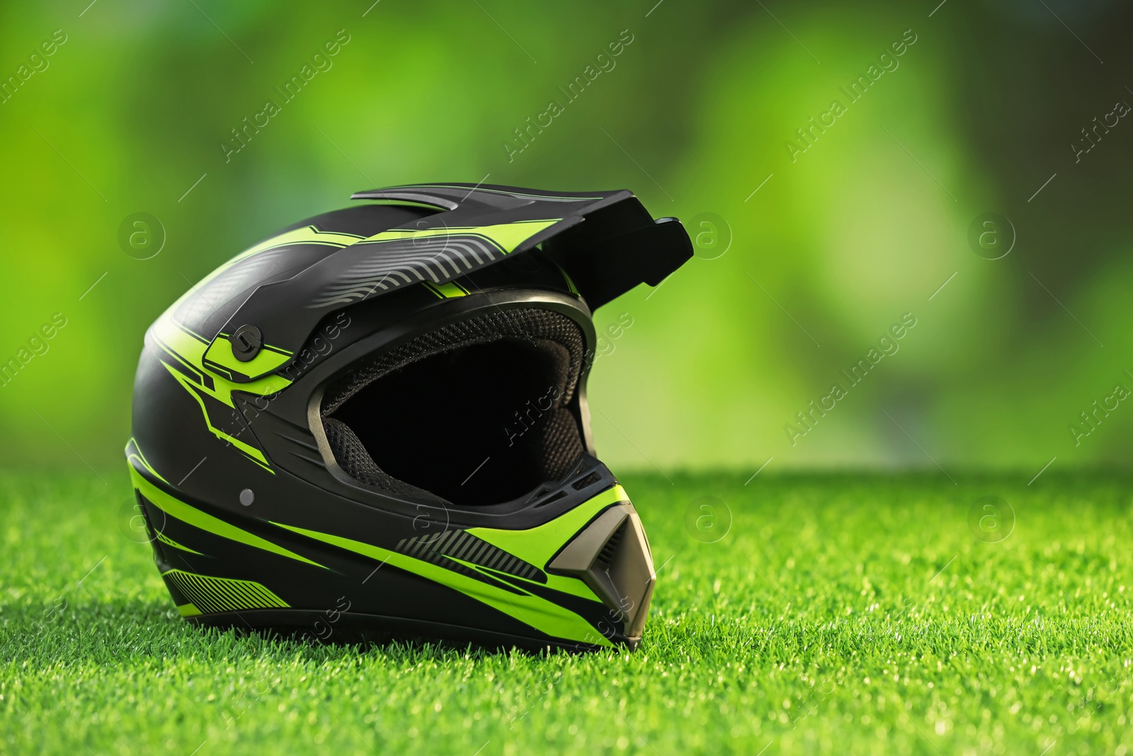 Photo of Modern motorcycle helmet with visor on green grass, space for text