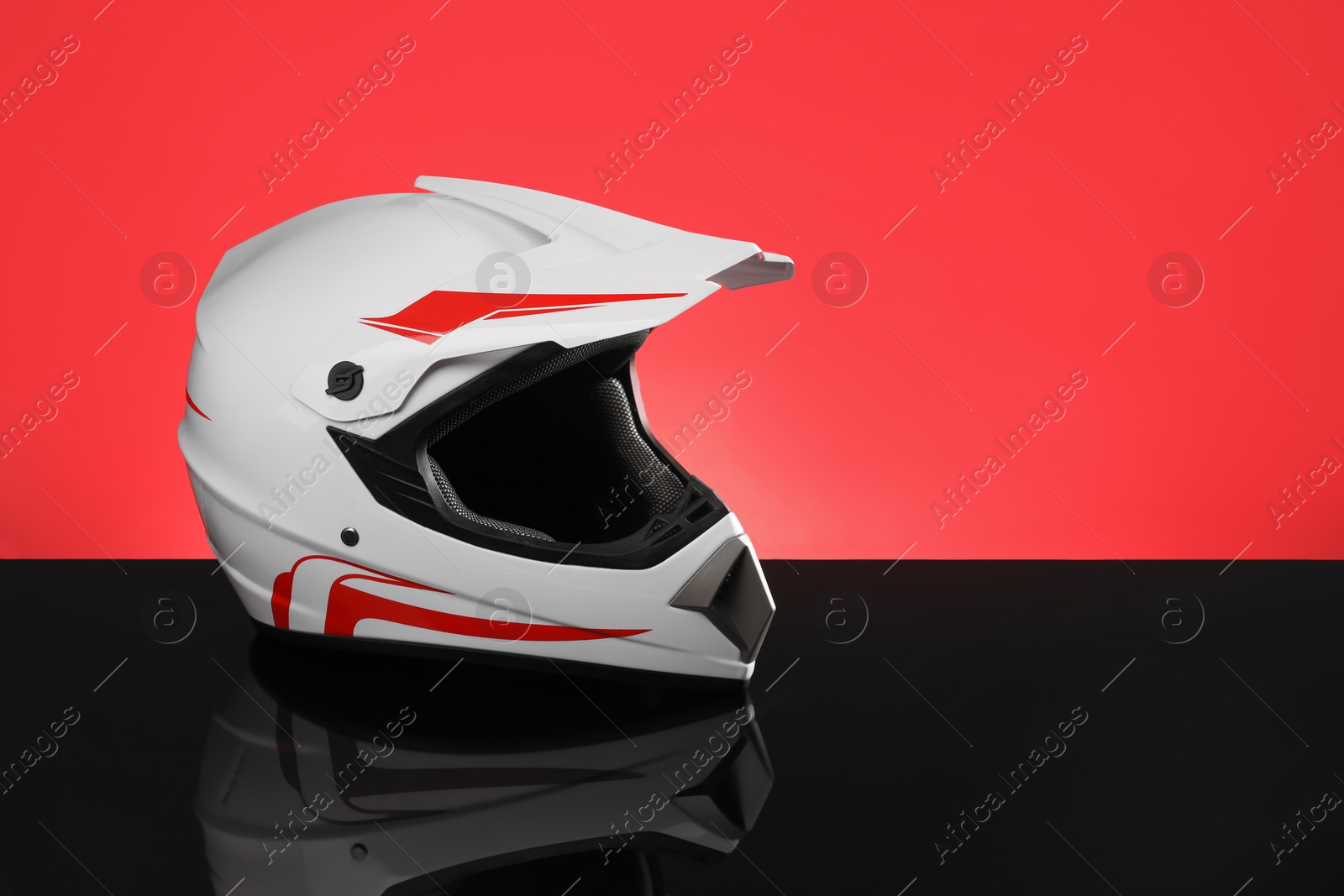 Photo of Modern motorcycle helmet with visor on mirror surface against red background. Space for text