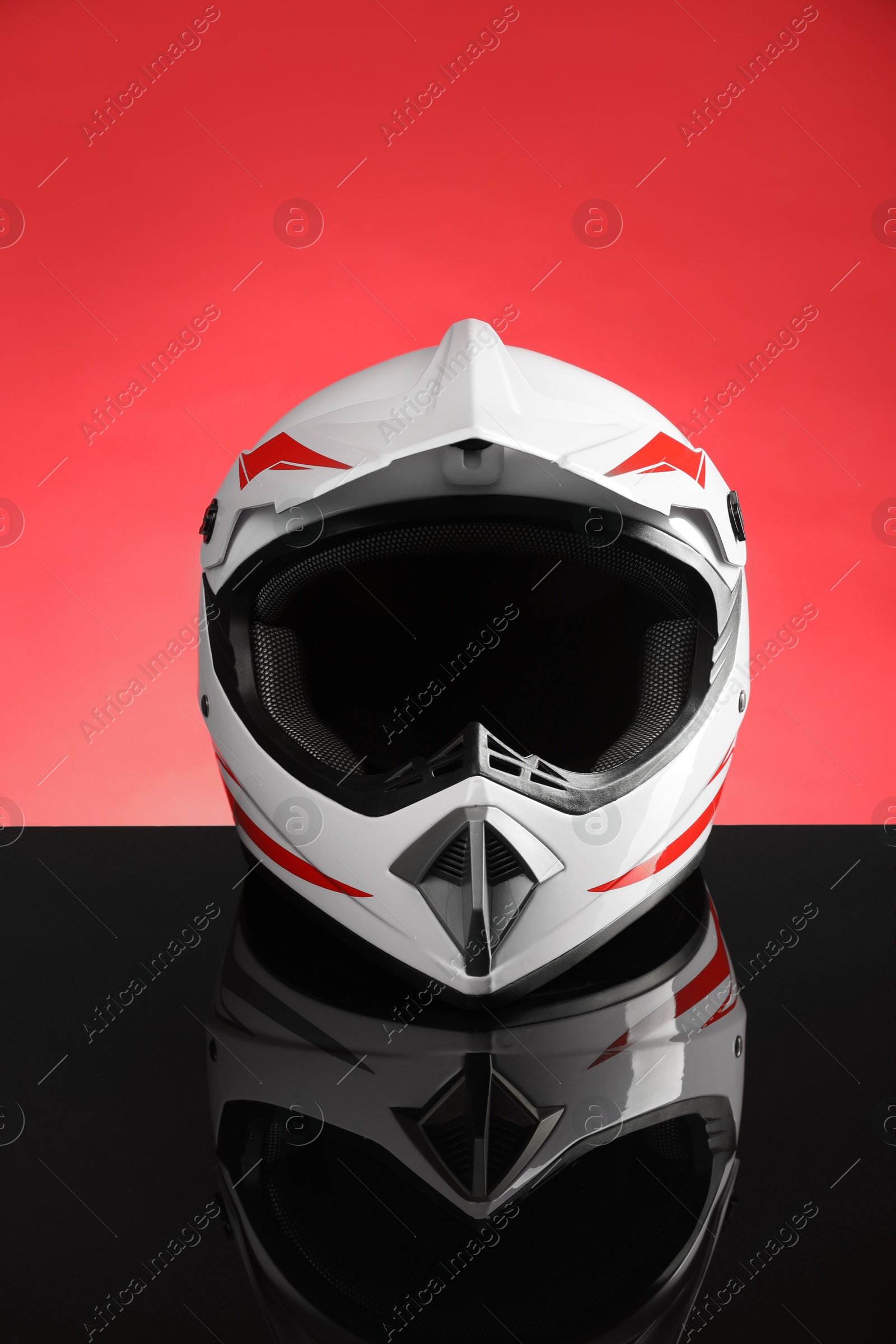 Photo of Modern motorcycle helmet with visor on mirror surface against red background