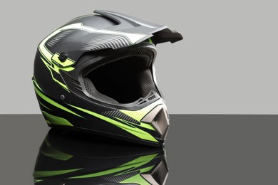 Photo of Modern motorcycle helmet with visor on mirror surface against light grey background. Space for text
