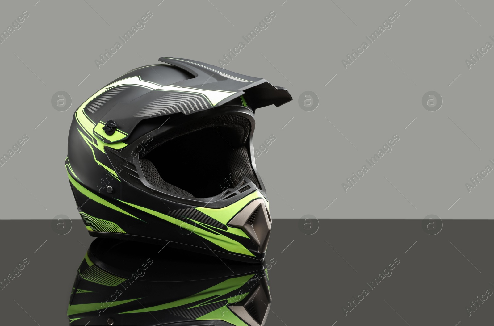 Photo of Modern motorcycle helmet with visor on mirror surface against light grey background. Space for text