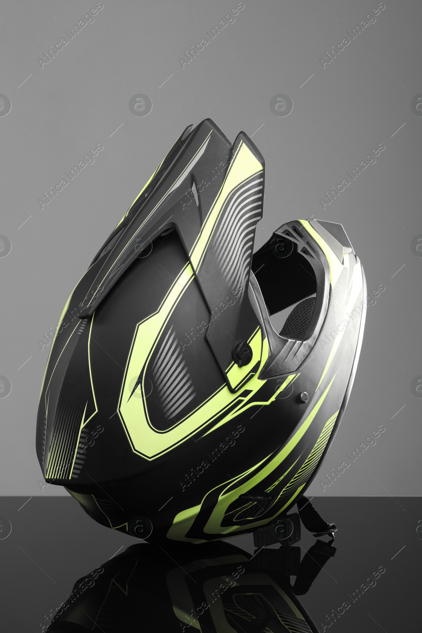 Photo of Modern motorcycle helmet with visor on mirror surface against light grey background