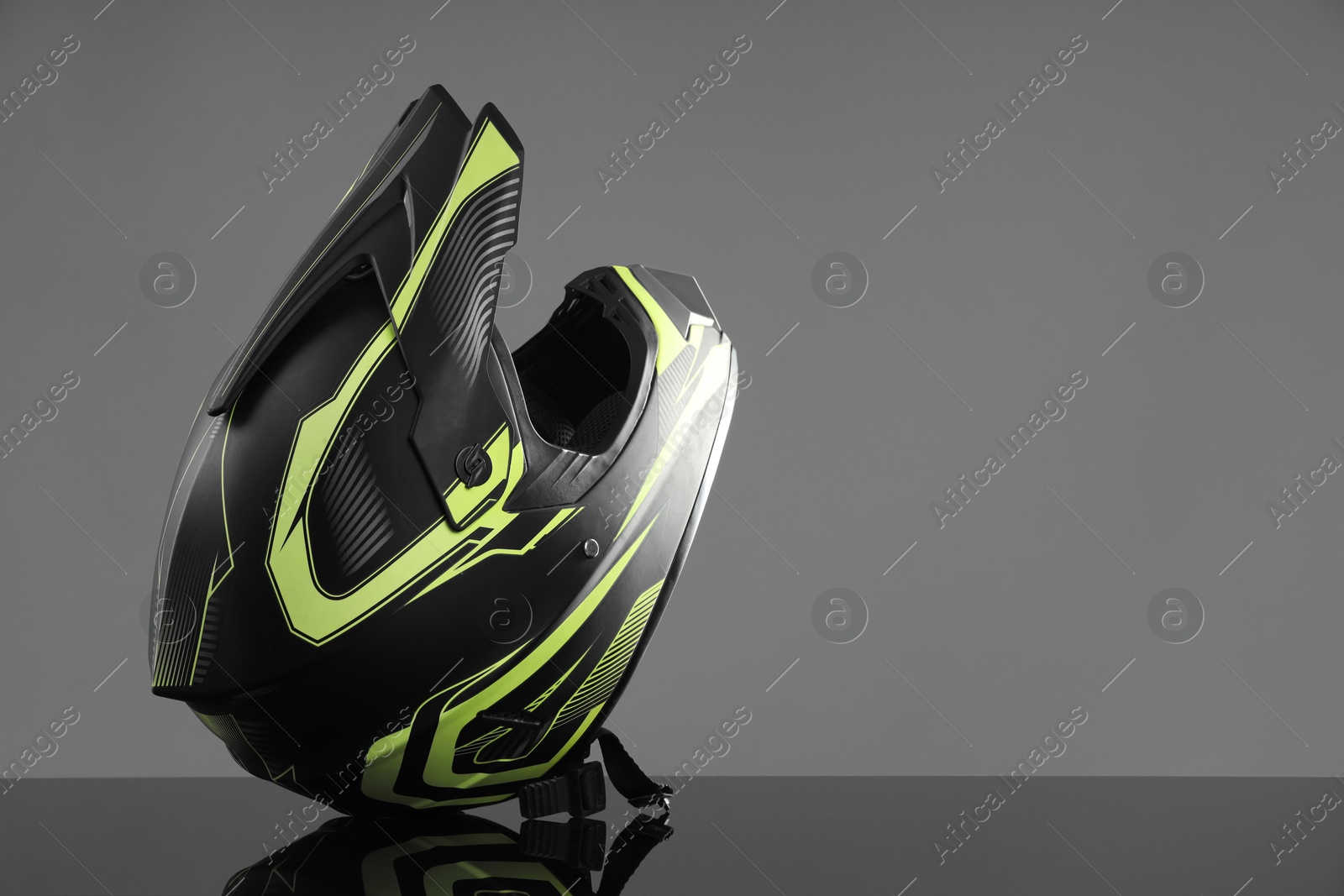 Photo of Modern motorcycle helmet with visor on mirror surface against light grey background. Space for text