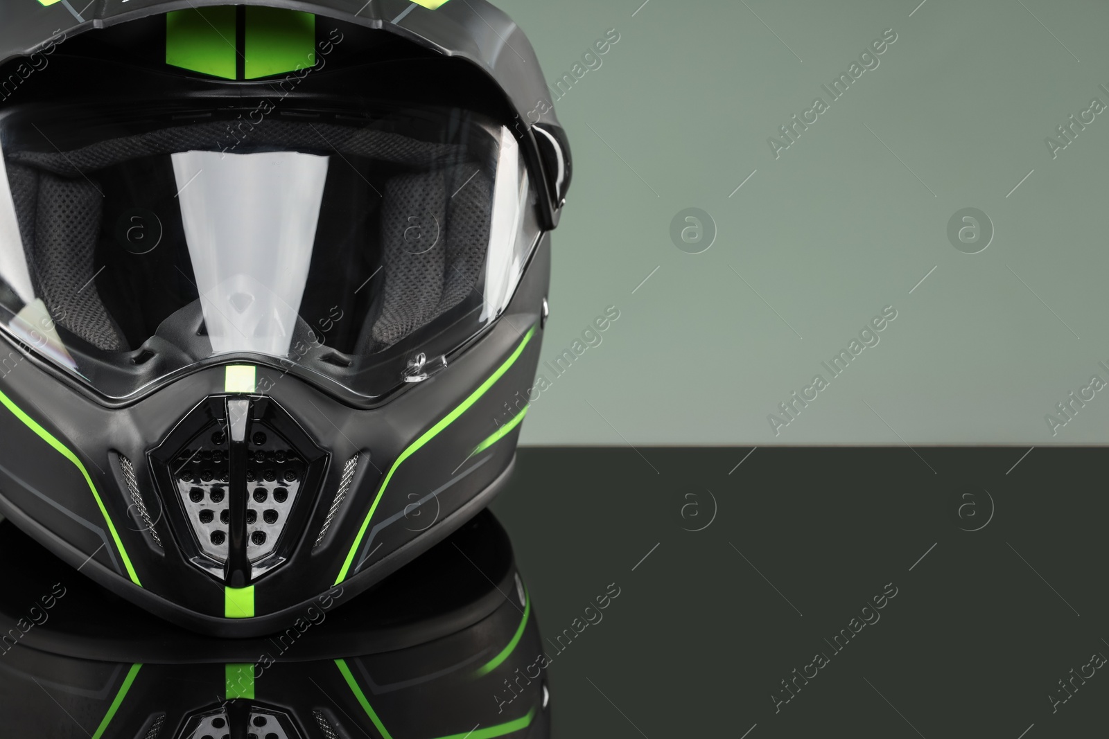 Photo of Modern motorcycle helmet with visor on mirror surface against light grey background, closeup. Space for text