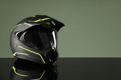 Photo of Modern motorcycle helmet with visor on mirror surface against light green background. Space for text