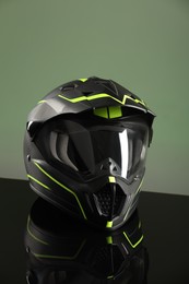 Photo of Modern motorcycle helmet with visor on mirror surface against light green background