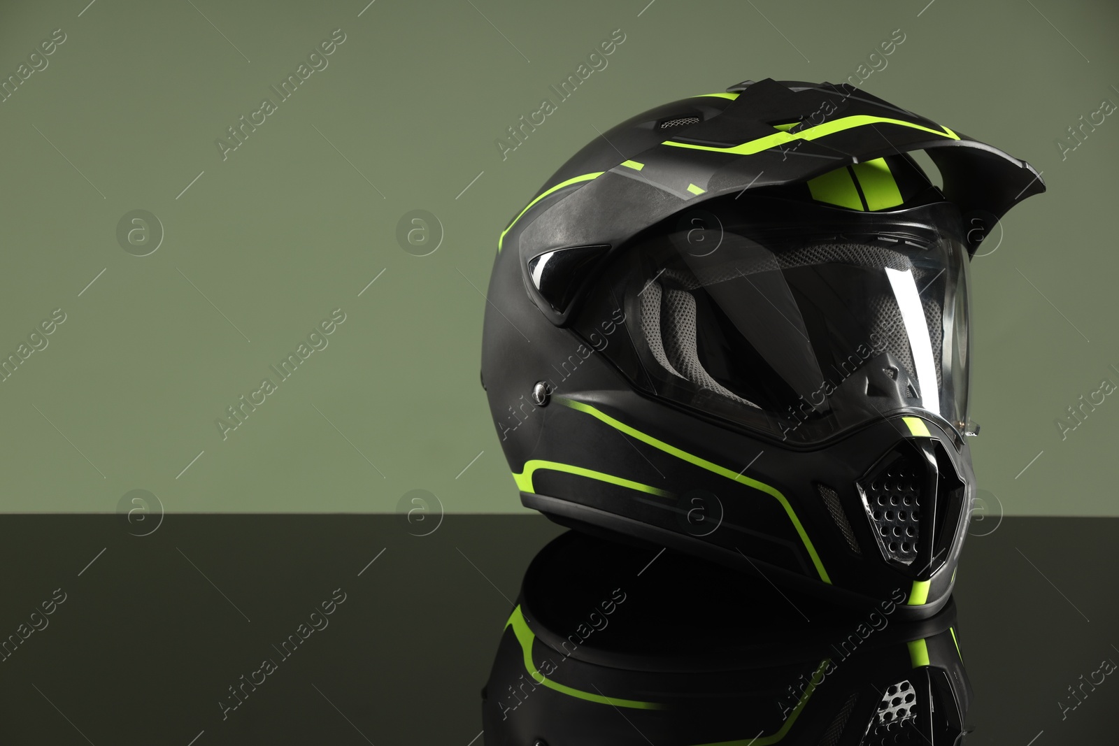 Photo of Modern motorcycle helmet with visor on mirror surface against light green background. Space for text