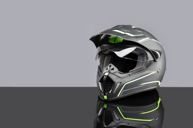 Photo of Modern motorcycle helmet with visor on mirror surface against light grey background. Space for text
