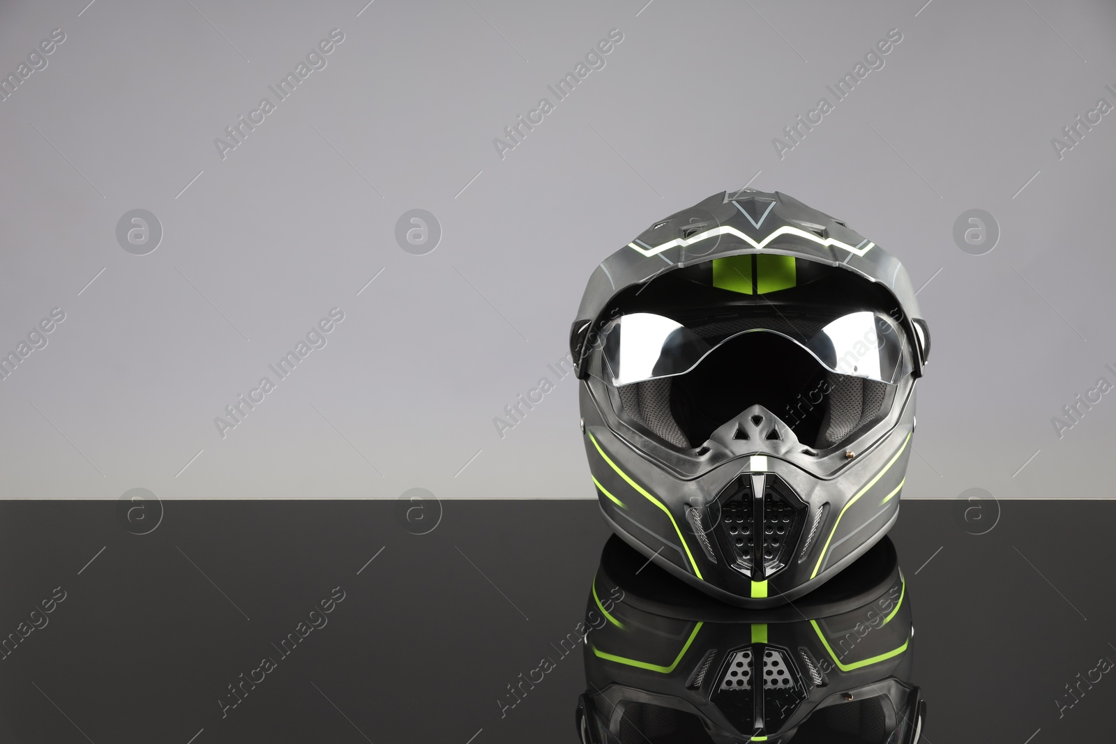 Photo of Modern motorcycle helmet with visor on mirror surface against light grey background. Space for text