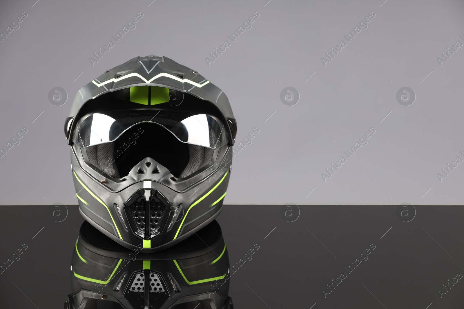 Photo of Modern motorcycle helmet with visor on mirror surface against light grey background. Space for text