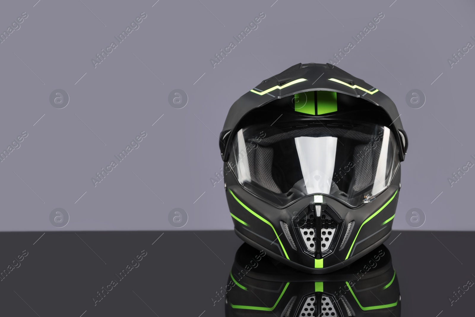 Photo of Modern motorcycle helmet with visor on mirror surface against light grey background. Space for text