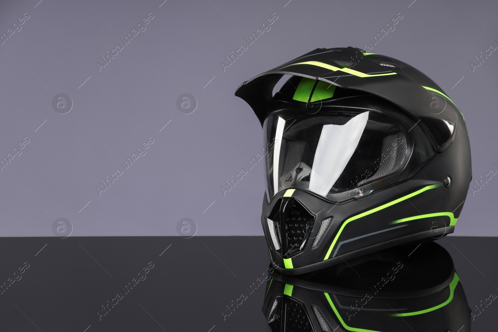 Photo of Modern motorcycle helmet with visor on mirror surface against light grey background. Space for text