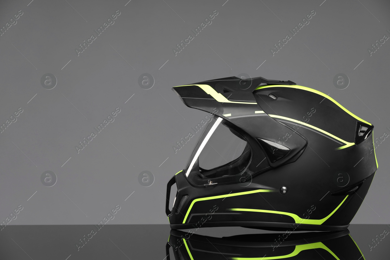 Photo of Modern motorcycle helmet with visor on mirror surface against light grey background. Space for text