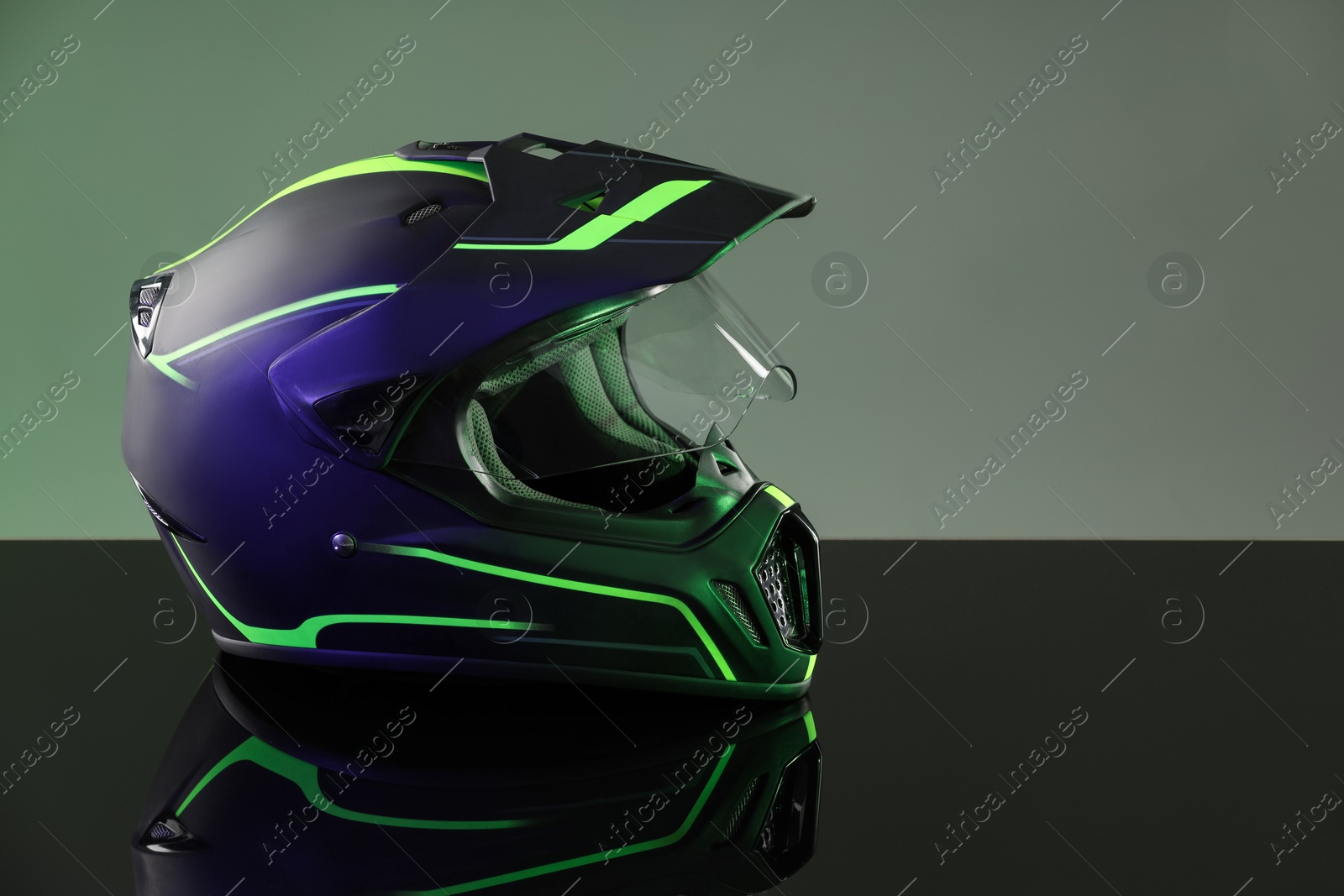 Photo of Modern motorcycle helmet with visor on mirror surface against grey background. Space for text