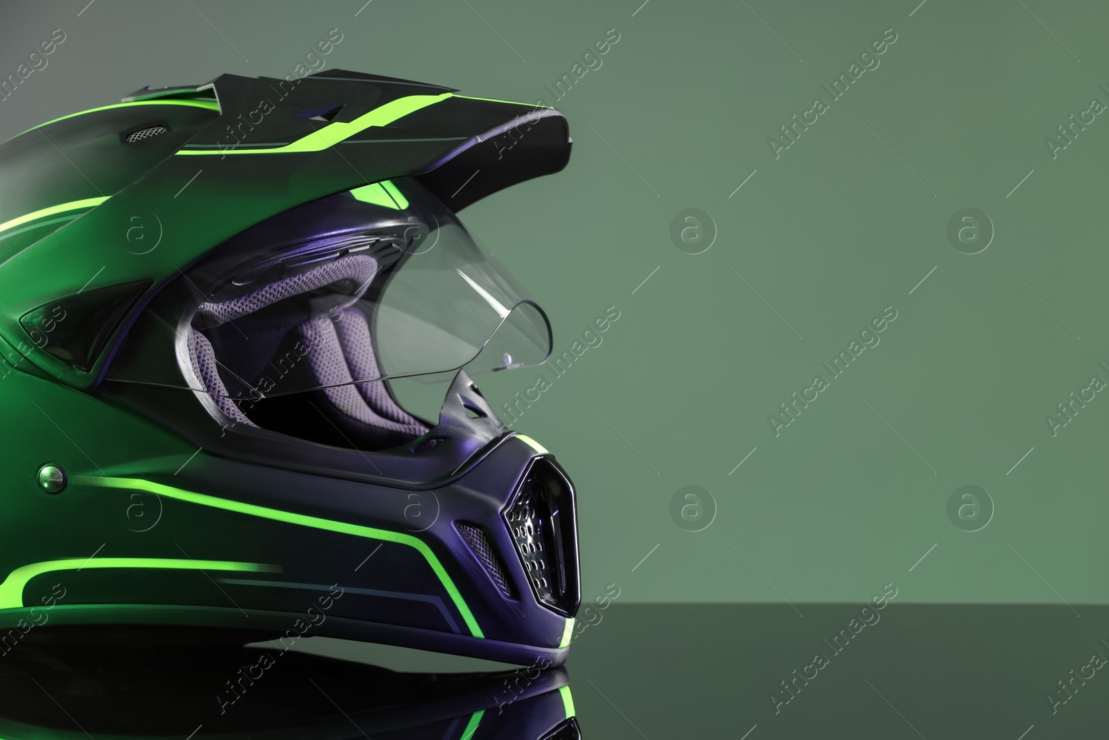 Photo of Modern motorcycle helmet with visor on mirror surface against grey background. Space for text