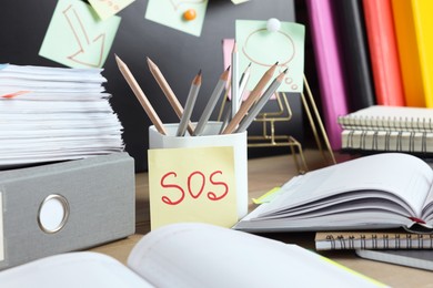 Photo of Sticky note with word SOS and stationery on table at workplace