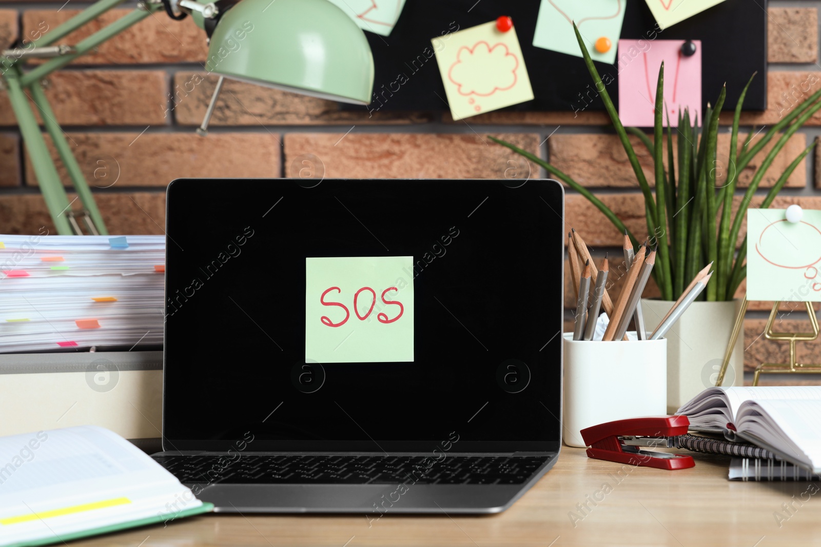 Photo of Sticky note with word SOS, laptop and stationery on wooden table at workplace