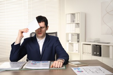 Photo of Embarrassed man with document at wooden table in office