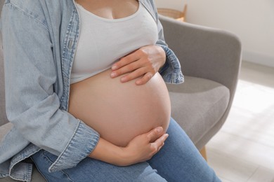 Pregnant woman sitting on sofa at home, closeup