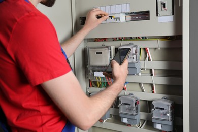 Technician worker with smartphone inspecting electricity meter, closeup