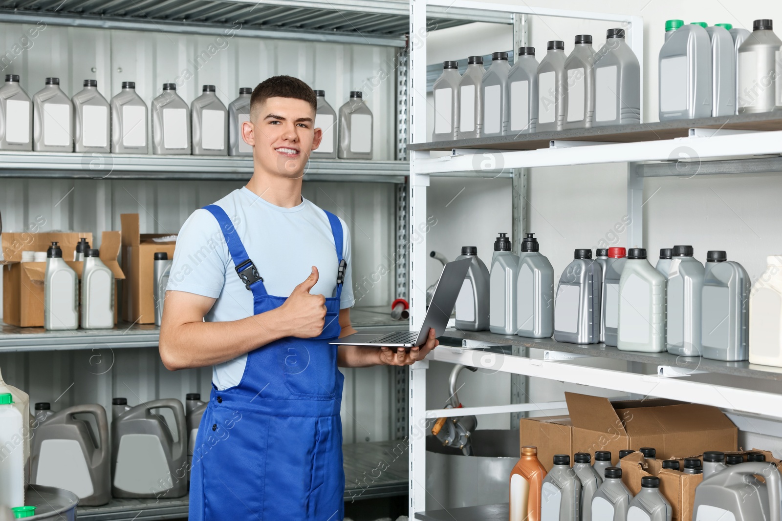 Photo of Smiling young man with laptop showing thumbs up in auto store with different car products