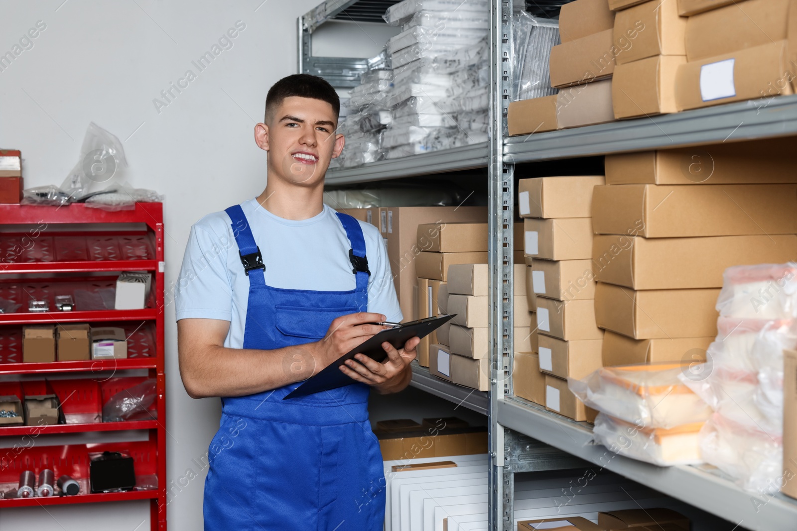 Photo of Smiling young man with clipboard near cardboard boxes in auto store