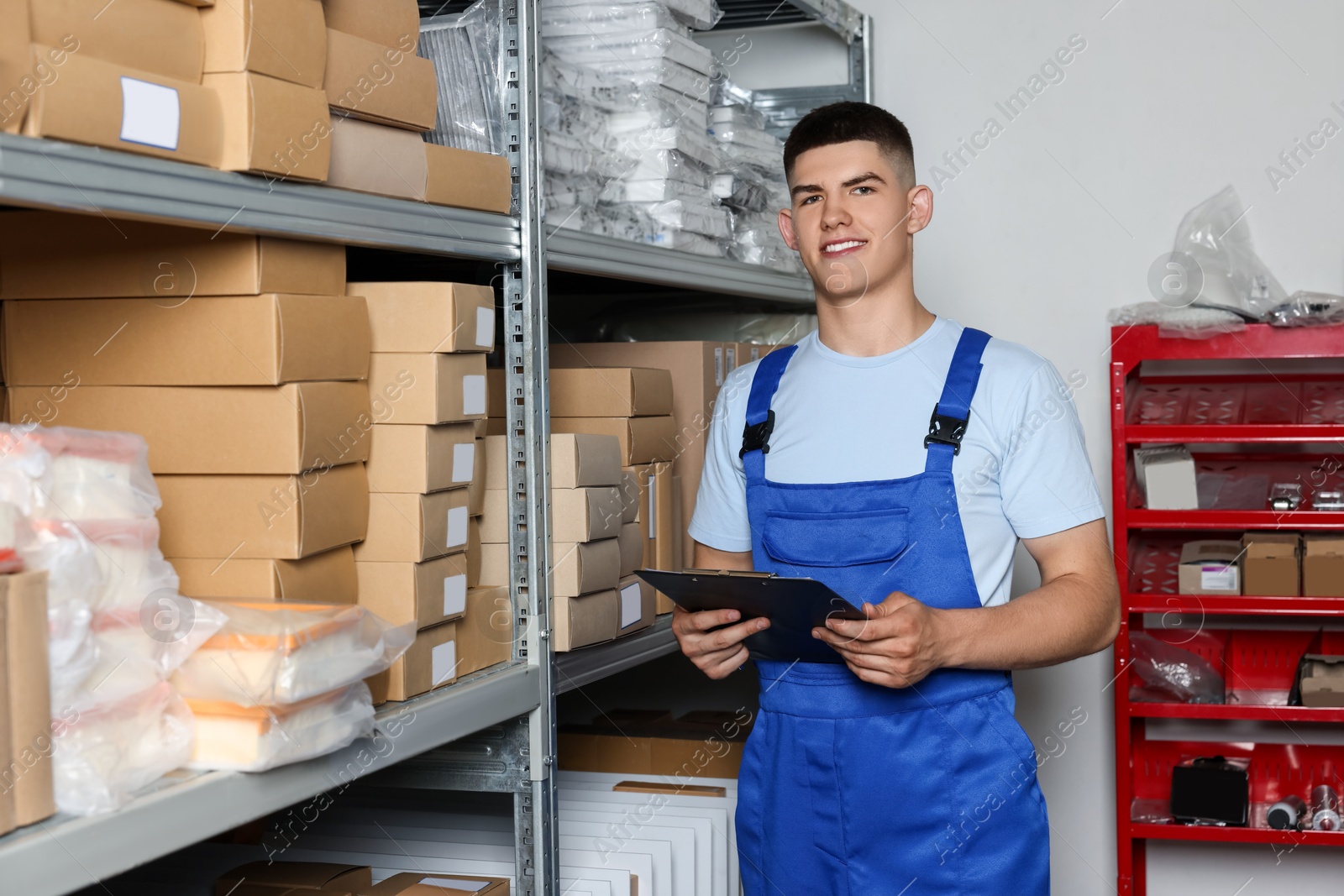 Photo of Smiling young man with clipboard near cardboard boxes in auto store