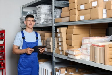 Photo of Smiling young man with clipboard near cardboard boxes in auto store