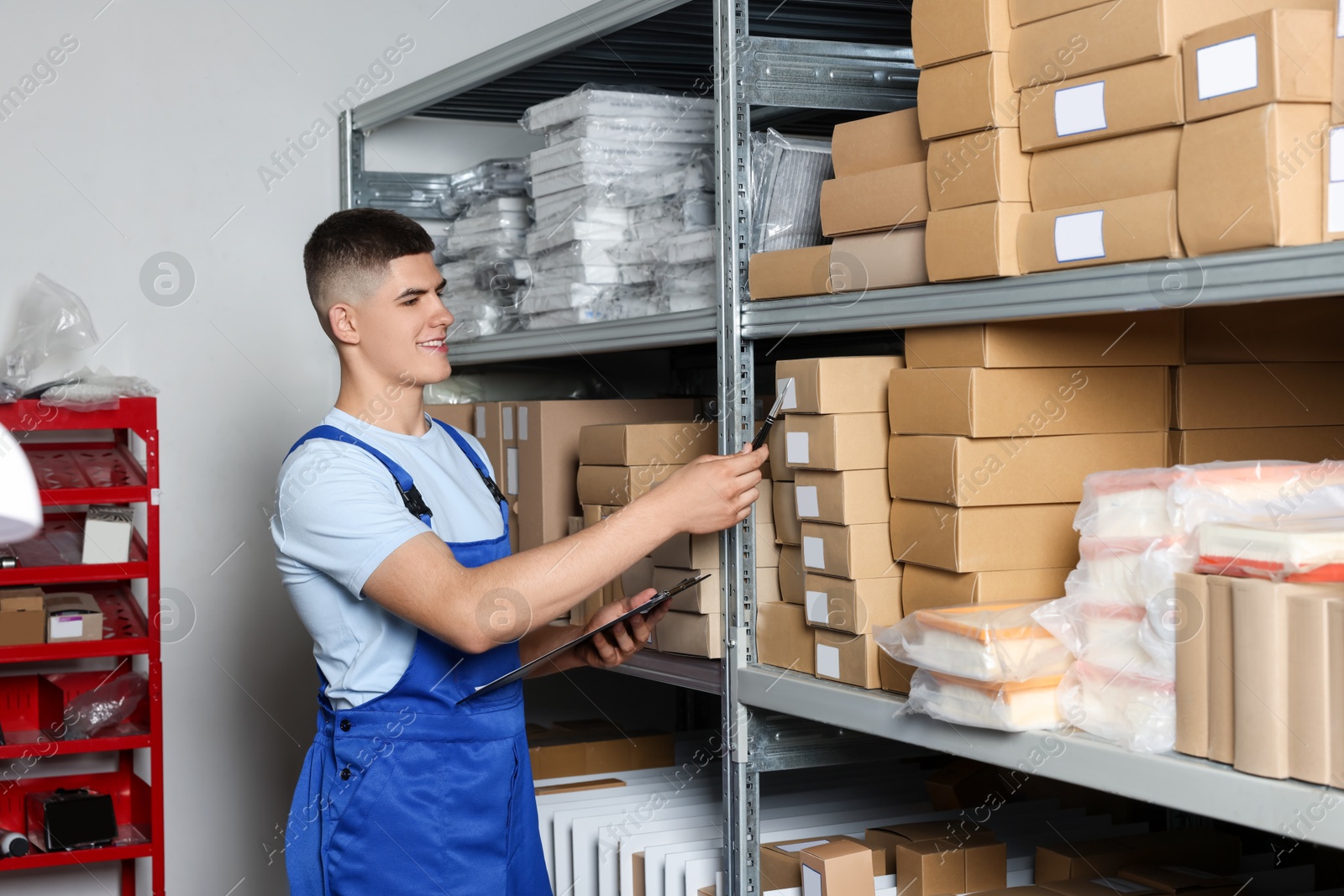 Photo of Smiling young man with pen and clipboard near cardboard boxes in auto store